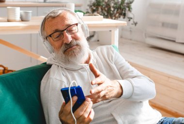 Yaşlı adam, havalı sakallı yaşlı adam video görüşmesi için cep telefonu kullanıyor. Mutluluk, yaşlılar yaşam tarzı kavramı. Akıllı telefondan çocuklara el sallayıp sohbet eden bir video. Modern.