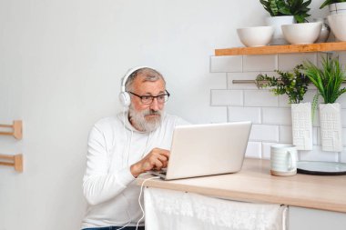 Kapüşonlu ve gözlüklü yakışıklı adam evde kanepede oturmuş müzik dinlerken dizüstü bilgisayar kullanıyor ve gülümsüyor.