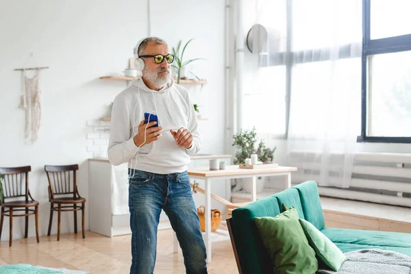 Stock image Senior man dance and using smartphone app for creating playlist music and - Elderly male having fun dancing with mobile phone technology