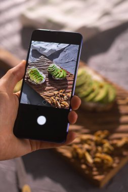 Smartphone alarak resimden organik sağlıklı sandviç. Kadın eli. Tablo farklı gıda ile yakın çekim.