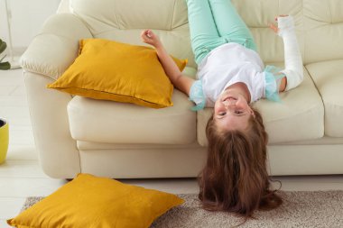 Kırık bileği ya da kolu olan bir çocuk gülümsüyor ve kanepede eğleniyor. Pozitif tutum, iyileşme ve çocuk.