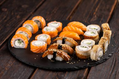 Large sushi set from top on black background. Assortment of various maki nigiri and rolls seafood soy sauce