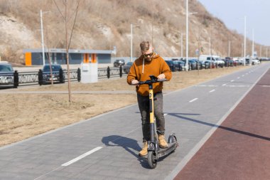 Şehirde elektrikli scooter kullandıktan sonra akıllı telefon kullanan sakallı hippi. Yenilikçi ulaşım