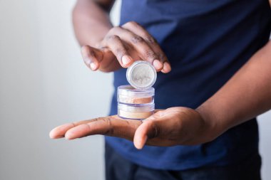 African american man holds mineral facial powder for perfect make-up for women - male make-up artist and cosmetic product
