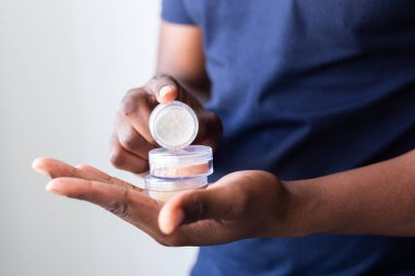 African american man holds mineral facial powder for perfect make-up for women - male make-up artist and cosmetic product