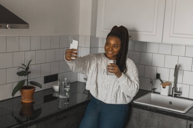 Happy modern African American young girl talking on video chat and sit home communication concept. Smiling hipster girl making self portrait on her telephone at home