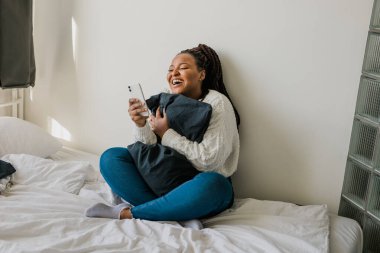 Happy modern African American young girl talking on video chat and sit home communication concept. Smiling hipster girl making self portrait on her telephone at home