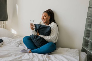 Happy modern African American young girl talking on video chat and sit home communication concept. Smiling hipster girl making self portrait on her telephone at home