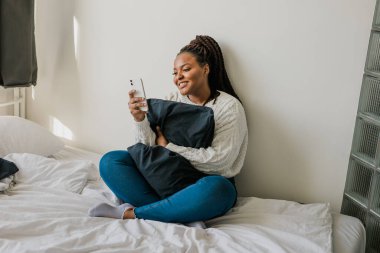 Happy modern African American young girl talking on video chat and sit home communication concept. Smiling hipster girl making self portrait on her telephone at home