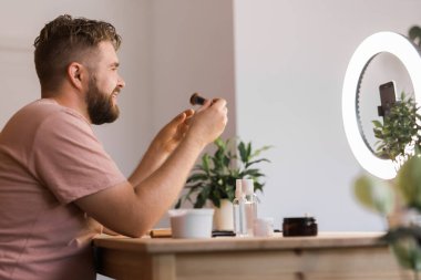 Ünlü blogcu. Video kaydederken kozmetik ürünlerini gösteren ve güzellik blogu için tavsiyelerde bulunan neşeli bir erkek vlogcu. Makyaj sanatçısı ve Güzellik vlog 'u