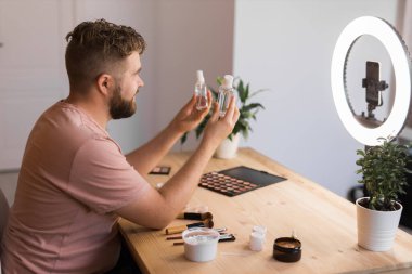Kozmetik ürünleri uygularken ya da kozmetik ürünleri incelerken video bloğu kaydeden adam. Kozmetik blogu için özel ders hazırlayan adam.