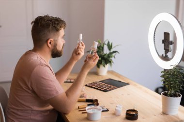 Ünlü blogcu. Video kaydederken kozmetik ürünlerini gösteren ve güzellik blogu için tavsiyelerde bulunan neşeli bir erkek vlogcu. Makyaj sanatçısı ve Güzellik vlog 'u