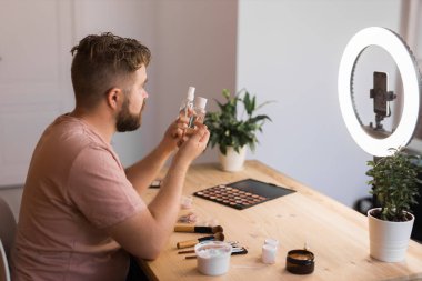 Kozmetik ürünleri uygularken ya da kozmetik ürünleri incelerken video bloğu kaydeden adam. Kozmetik blogu için özel ders hazırlayan adam.