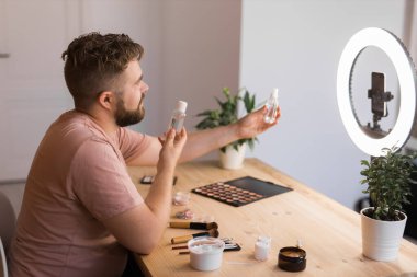 Makyaj ve güzellik ürünleri hakkında vlog yapan bir adam. Erkek, makyaj dersinde çekim yapıyor. Adamın biri onun telefonunu kullanarak makyaj dersi veriyor. Çeşitlilik ve blog yazarı.