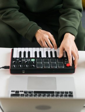 Recording electronic music track with portable midi keyboard on laptop computer in home studio. Producing and mixing music, beat making and arranging audio content with professional audio devices