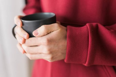 Close-up man with cup of coffee. Guy drinks coffee sitting near window.