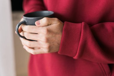 Close-up man with cup of coffee. Guy drinks coffee sitting near window.