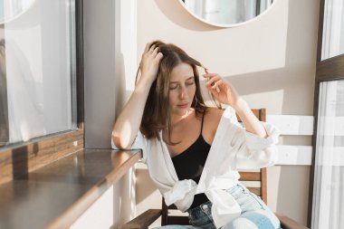 Pencerenin yanında, yüzünde çiçeklerin gölgesi olan güzel bir kadının portresi. Sabah ilkbahar estetiği