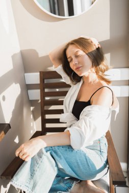 Happy young woman sit relaxing in comfortable chair feel peaceful enjoy sun near big windows. and smiling girl lying with eyes closed rest calm sunny morning at home.