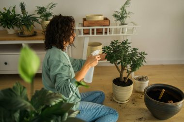Woman watering plants in home. Making homework. Domestic life