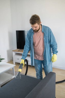 Man holding modern washing vacuum cleaner and cleaning dirty sofa with professionally detergent. Professional springclean at home