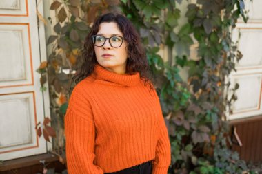 Portrait of carefree young woman smiling with urban background. Cheerful latin girl wearing eyeglasses in the city. Happy brunette woman with curly hair spectacles smiling.