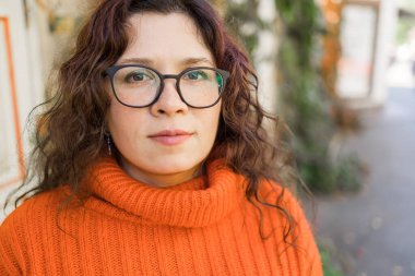 Portrait of carefree young woman smiling with urban background. Cheerful latin girl wearing eyeglasses in the city. Happy brunette woman with curly hair spectacles smiling.