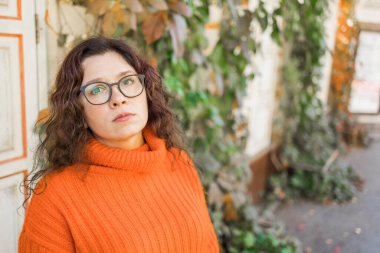 Portrait of carefree young woman smiling with urban background. Cheerful latin girl wearing eyeglasses in the city. Happy brunette woman with curly hair spectacles smiling.