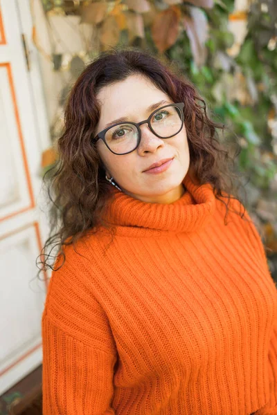一个戴着时髦眼镜 穿着针织时髦橙色毛衣 背景树叶的漂亮年轻女子的秋天肖像 女孩在城里散步 — 图库照片