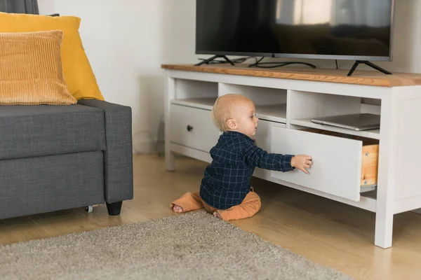 Stock image Toddler baby boy open cabinet drawer with his hand. Child explore what is in cabinet. Baby curiosity and child development stages concept