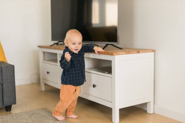 Caucasian baby newborn infant making first steps. Cute toddler kid child son boy learning walking creeping on living room. Childcare and childhood