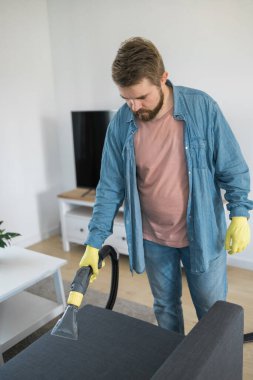 Man dry cleaners employee hand in protective rubber glove cleaning sofa with professionally extraction method. Early spring regular cleanup. Commercial cleaning company