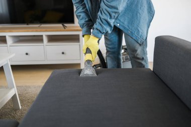 Man holding modern washing vacuum cleaner and cleaning dirty sofa with professionally detergent. Professional springclean at home