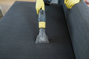 Man in protective rubber glove cleaning sofa with professionally extraction method with washing vacuum cleaner. Early spring regular cleanup. Commercial cleaning company