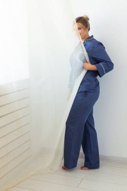 Gülümseyen sarışın kadın pijamayla oturma odasında rahat bir koç üzerinde oturuyor. Ev kıyafetleri ve evde boş zaman tatili.