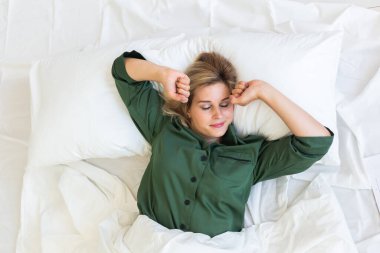 Güzel sarışın kadın sabah uyanır ve yatakta uzanır, genç kadın yeni günü selamlar.