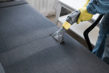 Man holding modern washing vacuum cleaner and cleaning dirty sofa with professionally detergent. Professional springclean at home