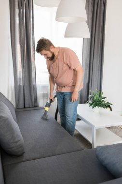 Man cleaning couch with washing vacuum cleaner