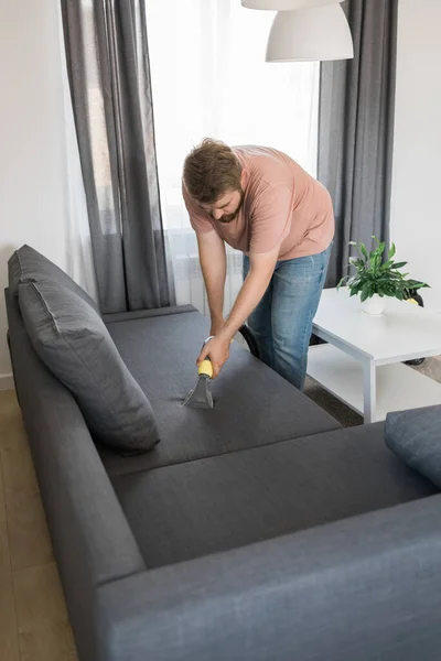 stock image Man holding modern washing vacuum cleaner and cleaning dirty sofa with professionally detergent. Professional springclean at home