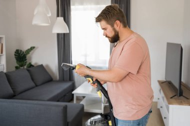 Man holding modern washing vacuum cleaner and cleaning dirty sofa with professionally detergent. Professional springclean at home