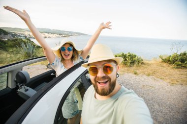 Romantik çift, okyanus ya da deniz kıyısındaki kiralık Cabrio arabasında akıllı telefon kamerasıyla selfie çekiyor, yaz tatilinin tadını çıkarıyor ve hafta sonları deniz kenarında cep telefonuyla dinlenirken fotoğraf çekiyor.