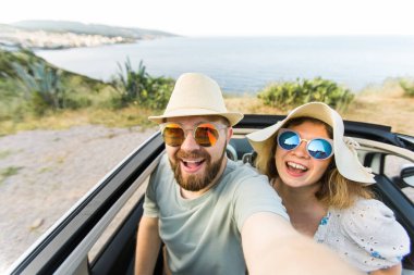 Romantik çift, okyanus ya da deniz kıyısındaki kiralık Cabrio arabasında akıllı telefon kamerasıyla selfie çekiyor, yaz tatilinin tadını çıkarıyor ve hafta sonları deniz kenarında cep telefonuyla dinlenirken fotoğraf çekiyor.