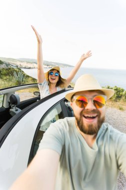 Romantik çift, okyanus ya da deniz kıyısındaki kiralık Cabrio arabasında akıllı telefon kamerasıyla selfie çekiyor, yaz tatilinin tadını çıkarıyor ve hafta sonları deniz kenarında cep telefonuyla dinlenirken fotoğraf çekiyor.