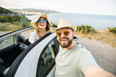 Mutlu ve güzel bir çift tatilde üstü açık bir arabayla selfie çektiriyorlar. Kiralık arabalar ve tatil konsepti