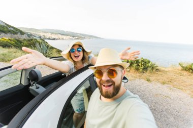 Mutlu ve güzel bir çift tatilde üstü açık bir arabayla selfie çektiriyorlar. Kiralık arabalar ve tatil konsepti