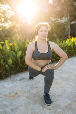 Genç, güzel, gülümseyen, spor bluzlu ve taytlı bir kadın yazın açık havada spor yapıyor.