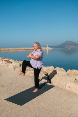 Rasta saçlı olgun bir kadın deniz sahilinde yoga egzersizi yapıyor. Sağlık ve aktif yaşlılık.