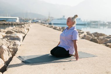 Rasta saçlı olgun bir kadın deniz sahilinde yoga egzersizi yapıyor. Sağlık ve aktif yaşlılık.