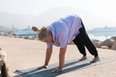 Rasta saçlı olgun bir kadın deniz sahilinde yoga egzersizi yapıyor. Sağlık ve aktif yaşlılık.