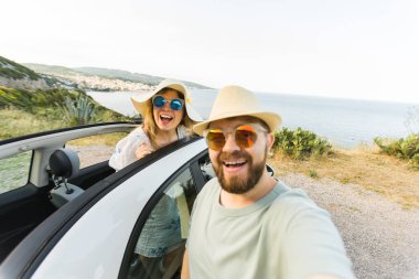 Mutlu ve güzel bir çift tatilde üstü açık bir arabayla selfie çektiriyorlar. Kiralık arabalar ve tatil konsepti